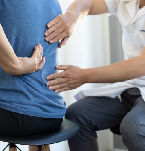 The doctor is diagnosing the patient's back pain. A male with back pain sees a doctor for treatment.